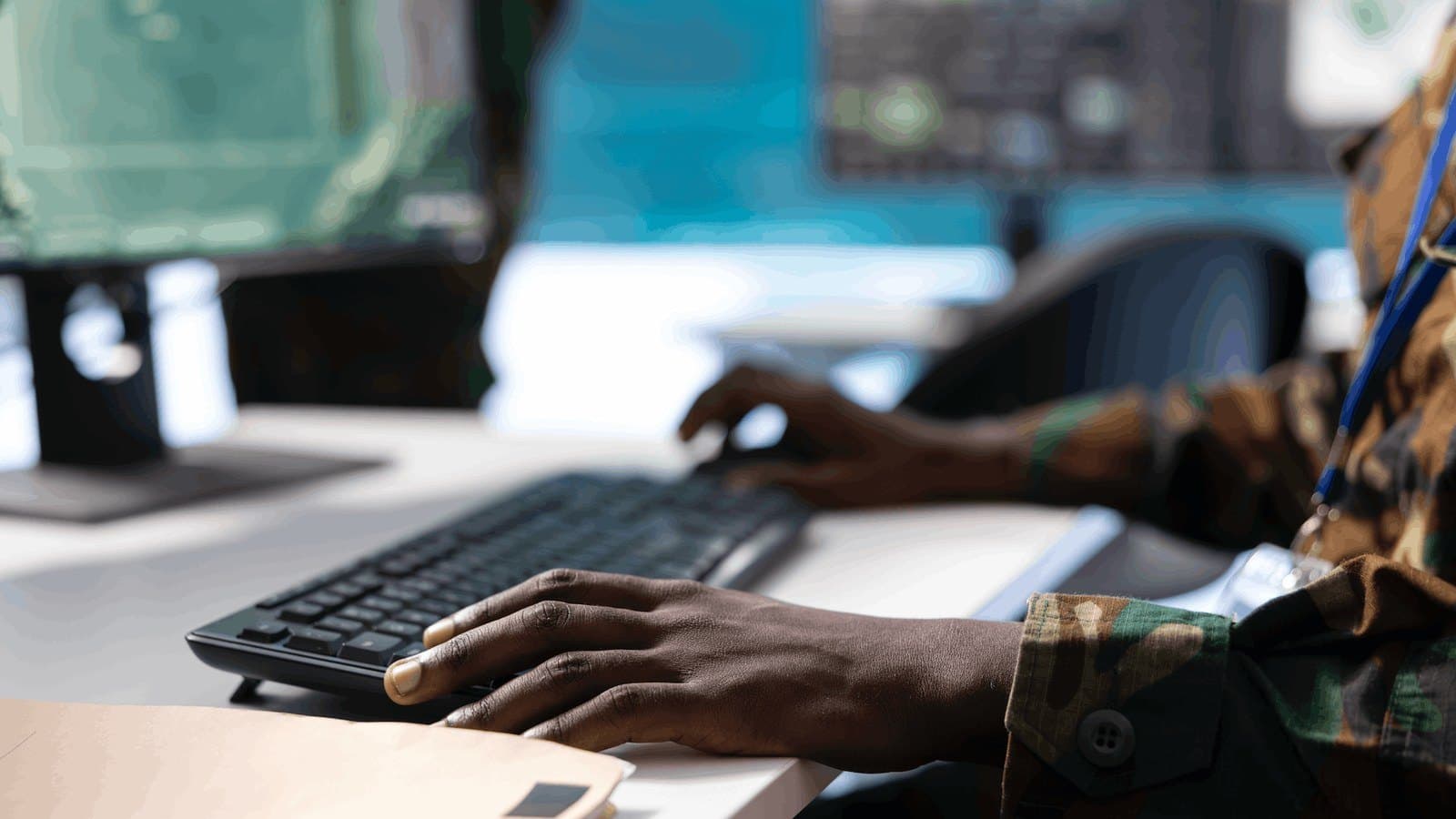 A service member in camouflage uniform working at a keyboard in an operations room, with screens in the background. Photo d'archive.