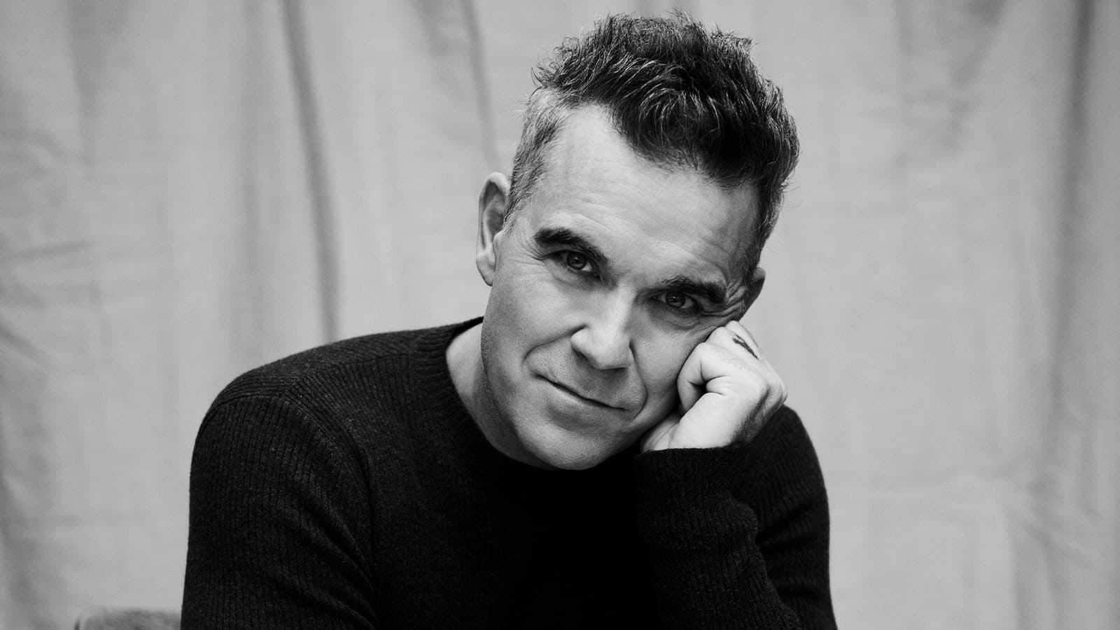 Robbie Williams photographed in black and white, resting his head on one hand. Photo d'archive.
