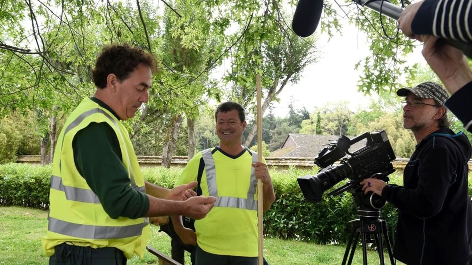 Two performers in high-visibility council workwear filmed by a camera operator outdoors. Archive photograph. Photo d'archive.