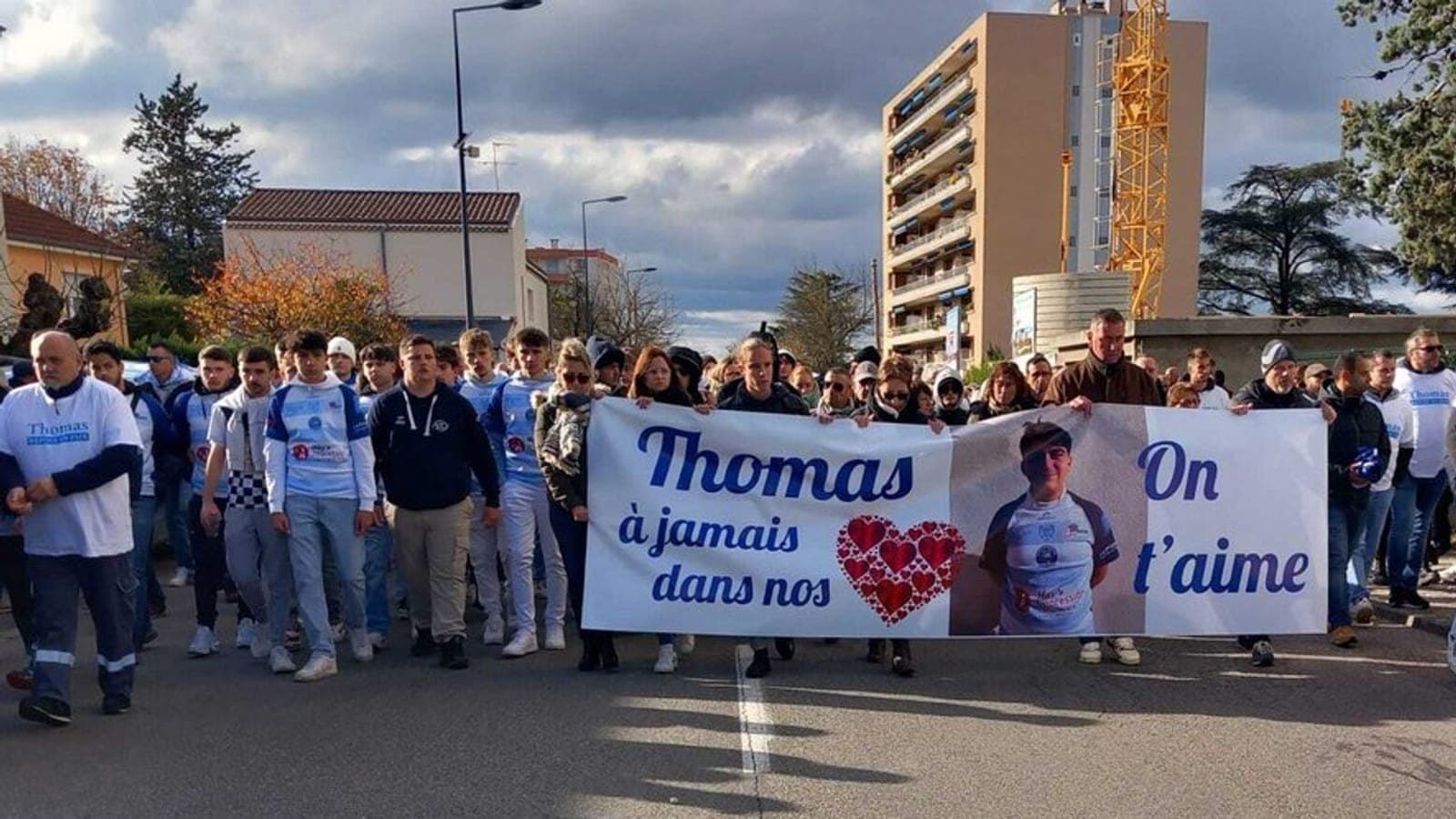 A silent march for Thomas Perotto, mourners walking behind a banner bearing his name and photograph.