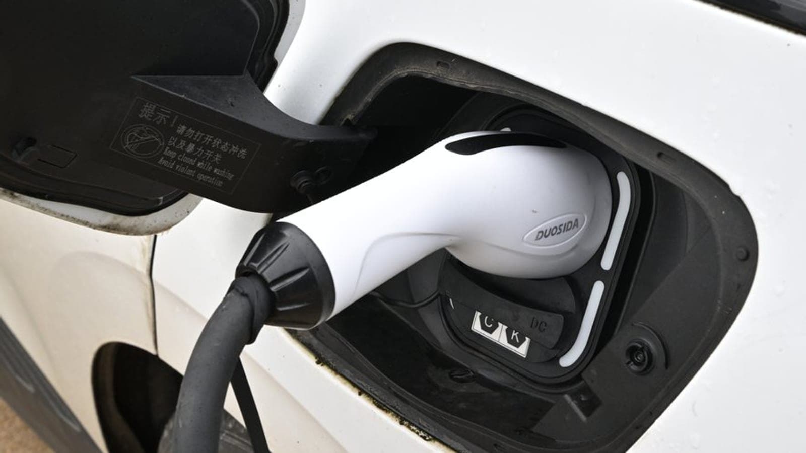 A charging connector plugged into the socket of a white electric car.