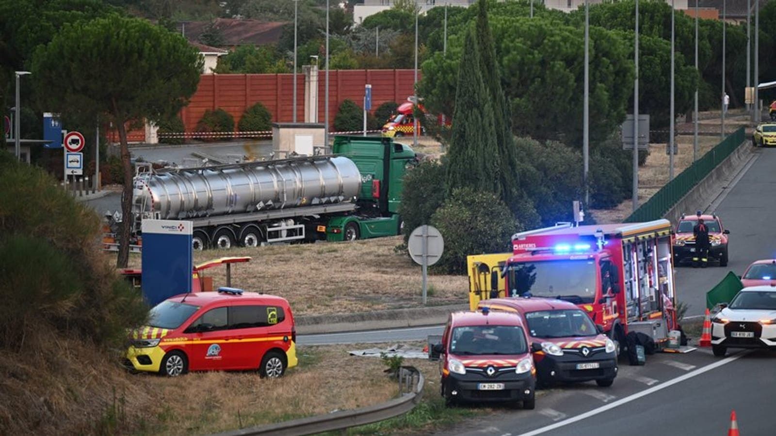 Un camion-citerne immobilisé près d'un péage, avec des véhicules de pompiers et un périmètre de sécurité au premier plan.