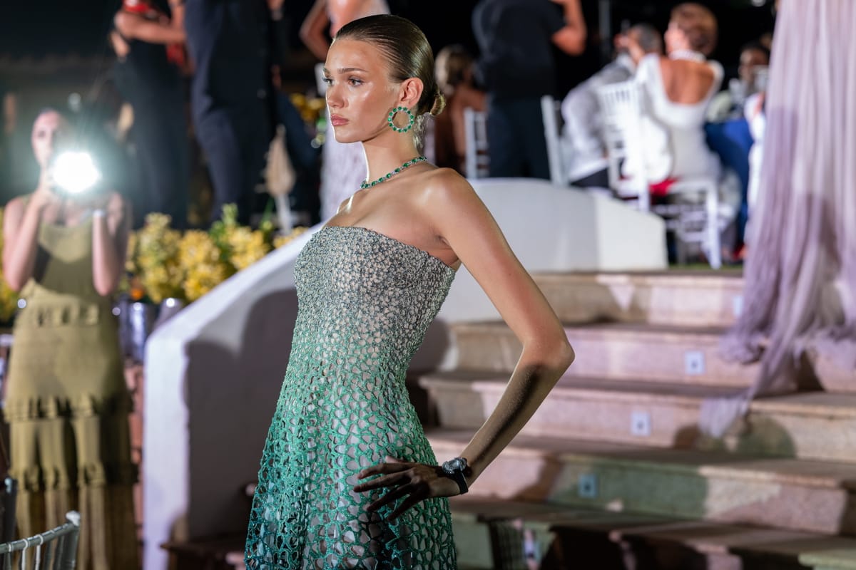 A model in a beaded gown and emerald jewellery on the runway beside the pool.