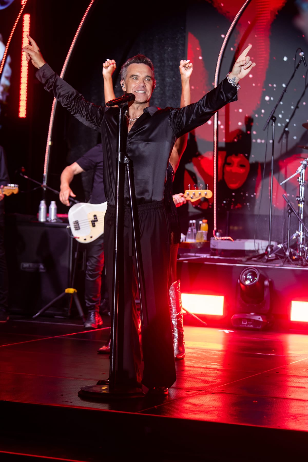 Robbie Williams at the microphone under red stage lighting.