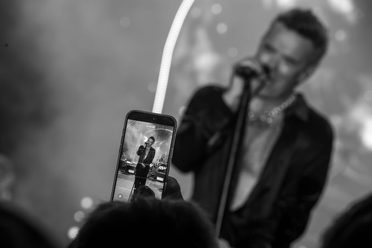 A guest filming Robbie Williams on a phone during the performance, in black and white.